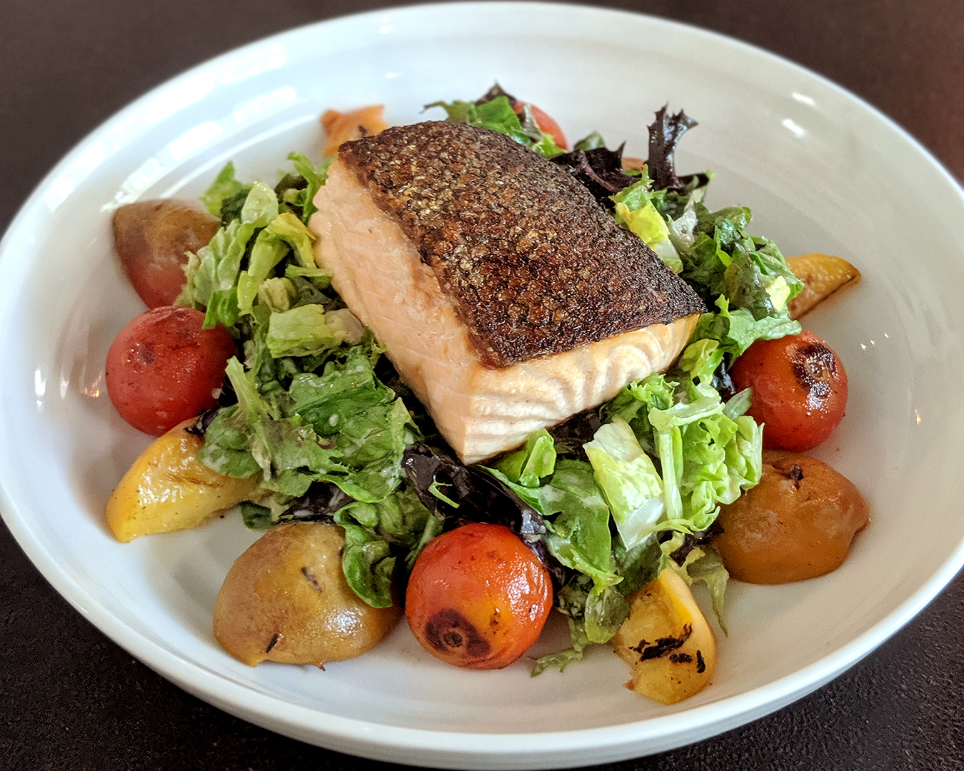 Salmon on a bed of lettuce surrounded by blistered cherry tomatoes and sliced grilled peaches