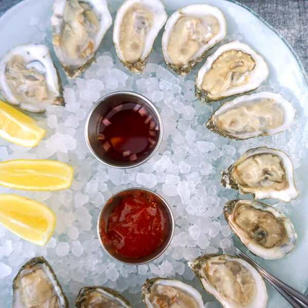 Raw oysters on the half-shell on plate of ice with lemon and sauce